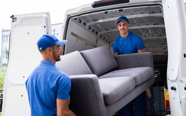 Twee bezorgers schuiven een grijze bank in een witte bestelbus