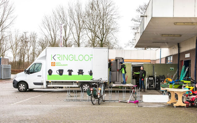 Een kringloopbus met uitgestalde spullen voor een gebouw