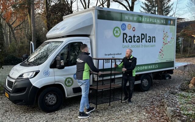 Twee medewerkers laden een aanhanger achter een bus van een kringloopbedrijf