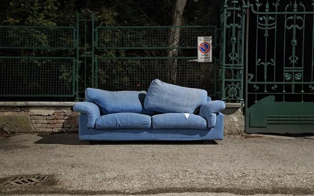 Een blauwe tweezitsbank tegen een hek langs de weg