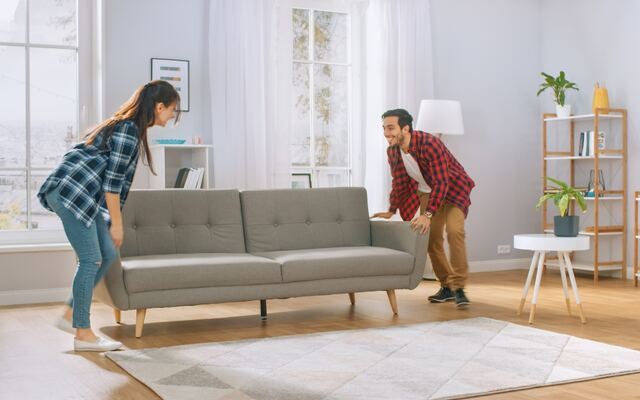 Twee mensen schuiven samen een bank door een lichte woonkamer