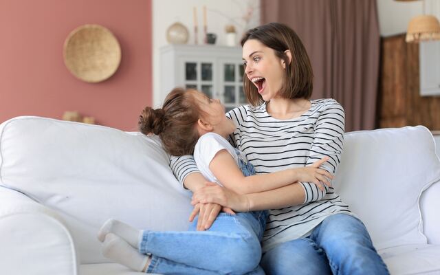 Een moeder en haar kind lachen samen op een witte bank